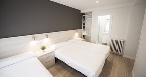 A modern bedroom with two beds, a bedside table with a lamp, a small plant, and a walk-in closet with a ladder. - Happy Hostal Carrales (Burgos)