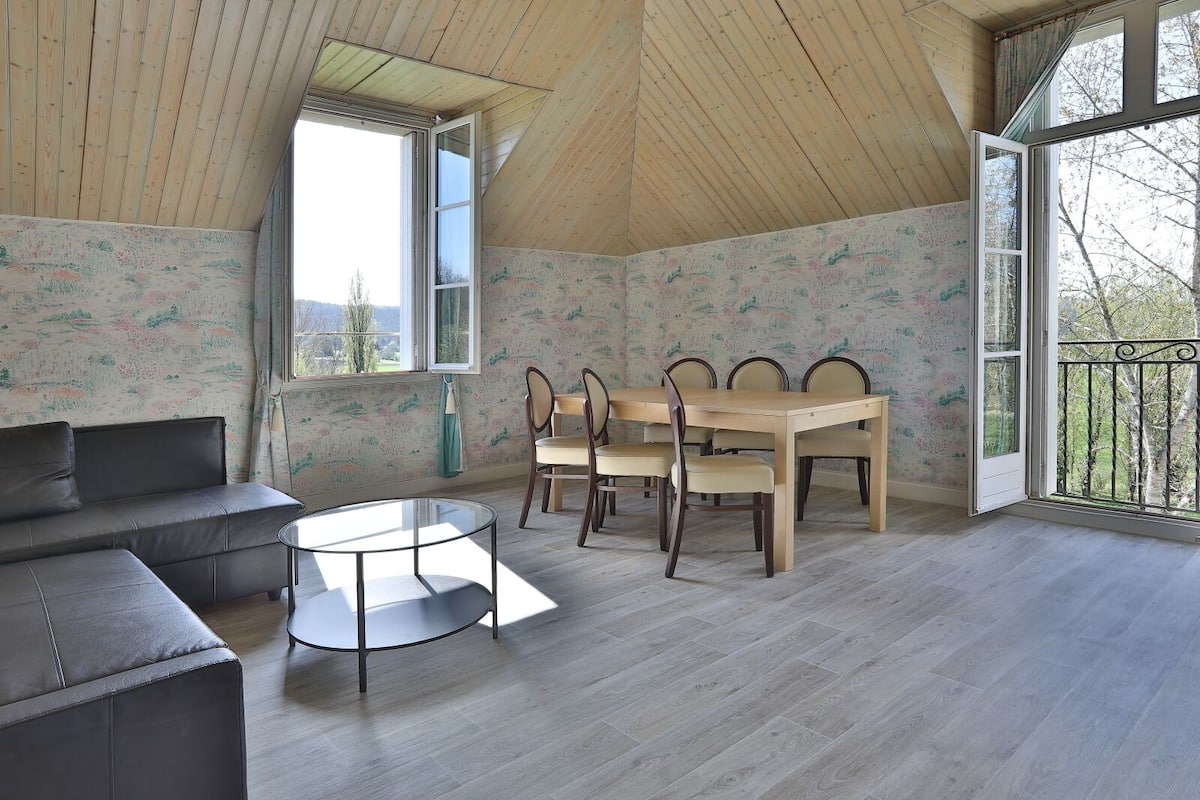 A room with a wooden ceiling, a dining table with chairs, a sofa, and a round glass table.