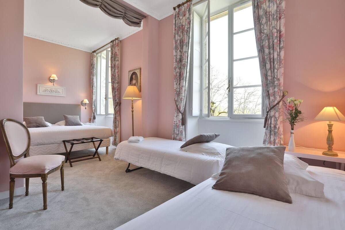 A hotel room with two single beds, a chair, a small table, and a window with curtains.
