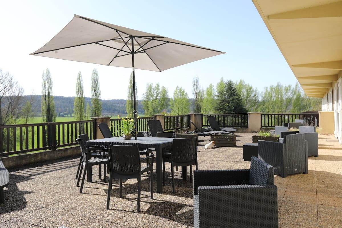 An outdoor patio with a table and chairs, a large umbrella, and a view of the surrounding landscape.