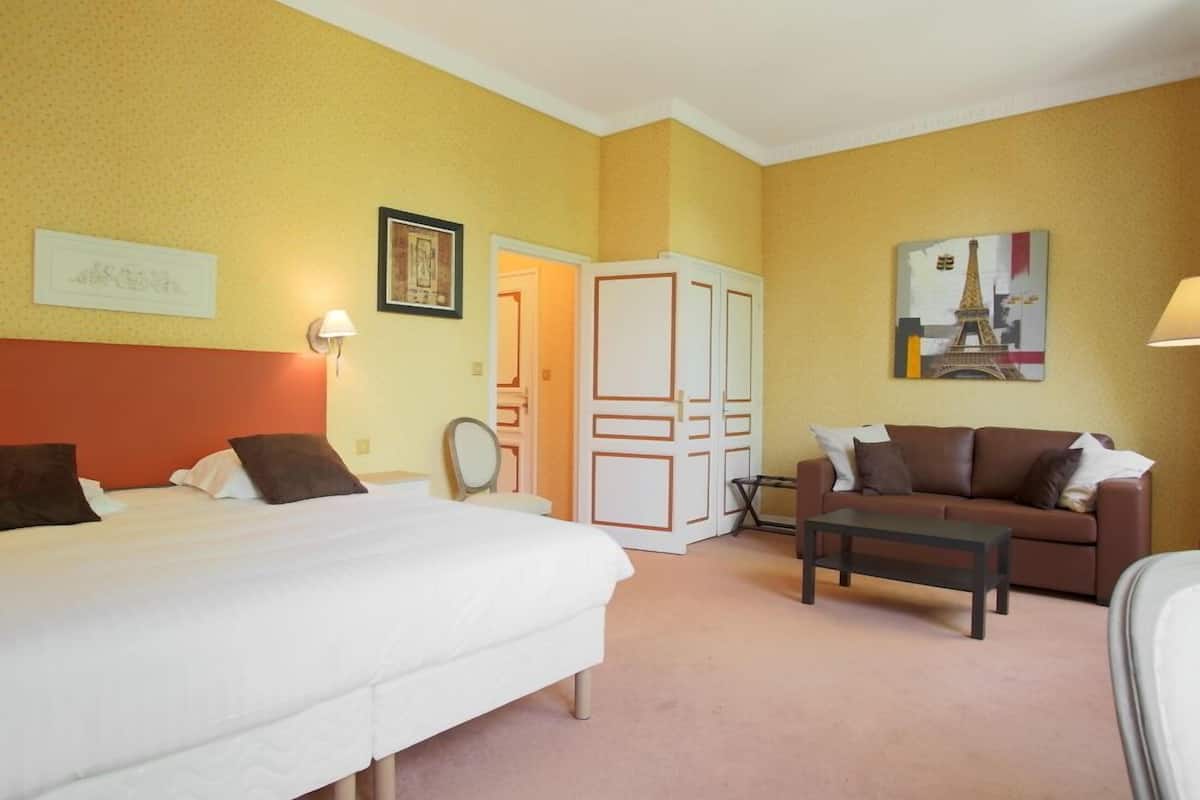 A hotel room with a bed, a sofa, a small table, and a wardrobe.