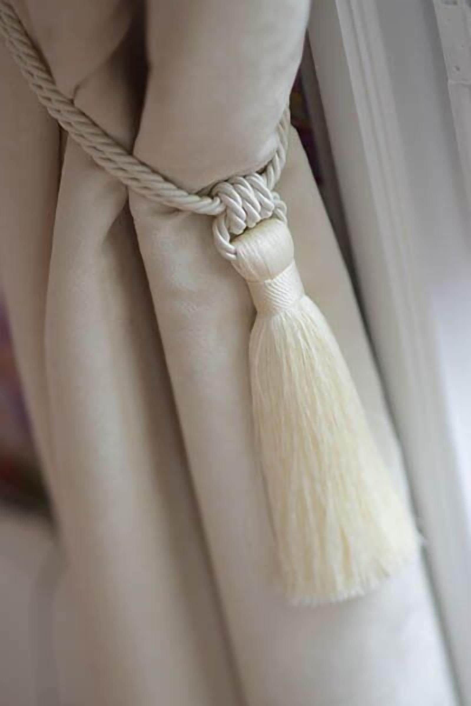 A close-up of a white rope with a tassel tied to a white object.