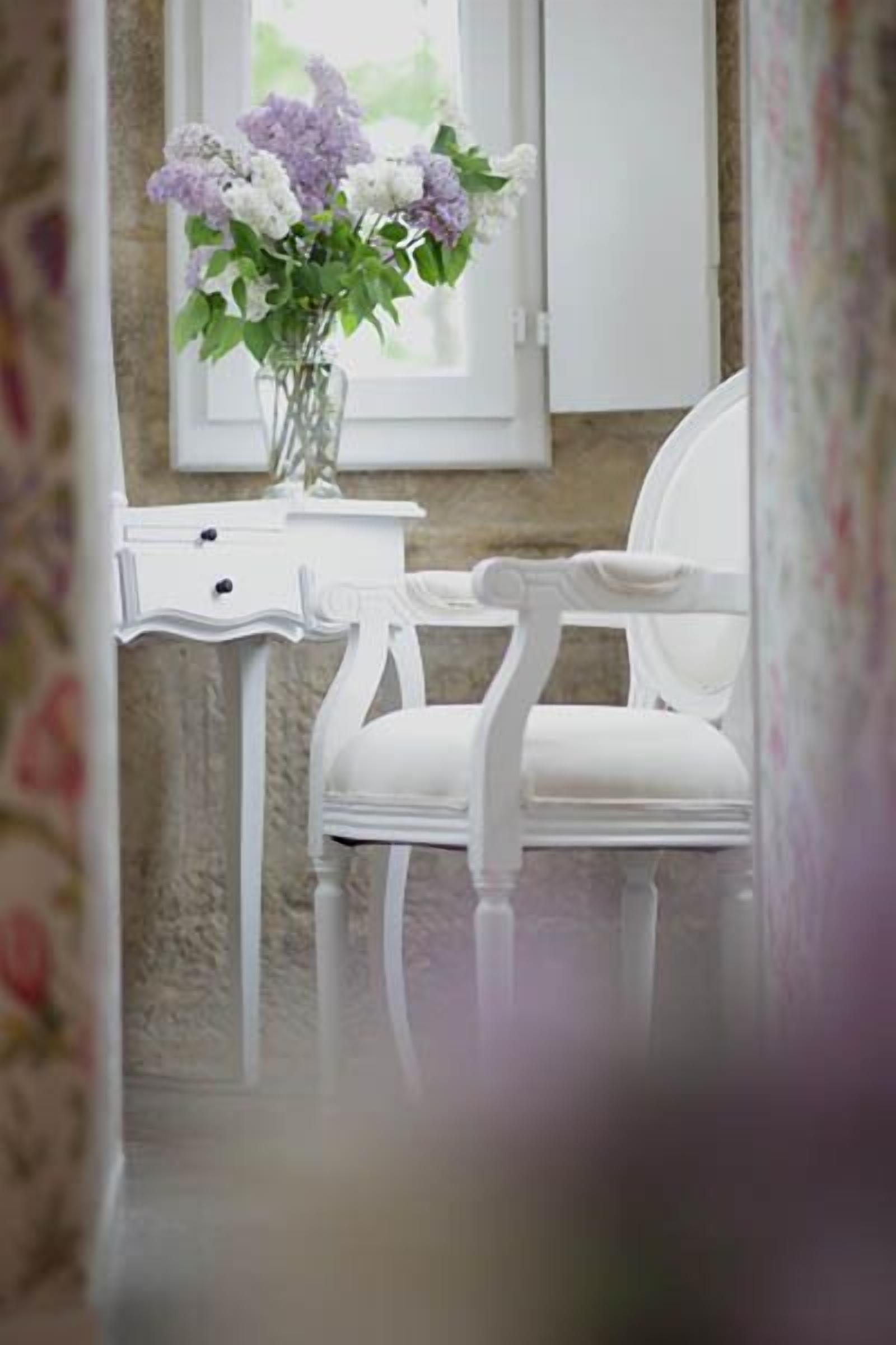 A white chair with a vase of flowers on a white table.