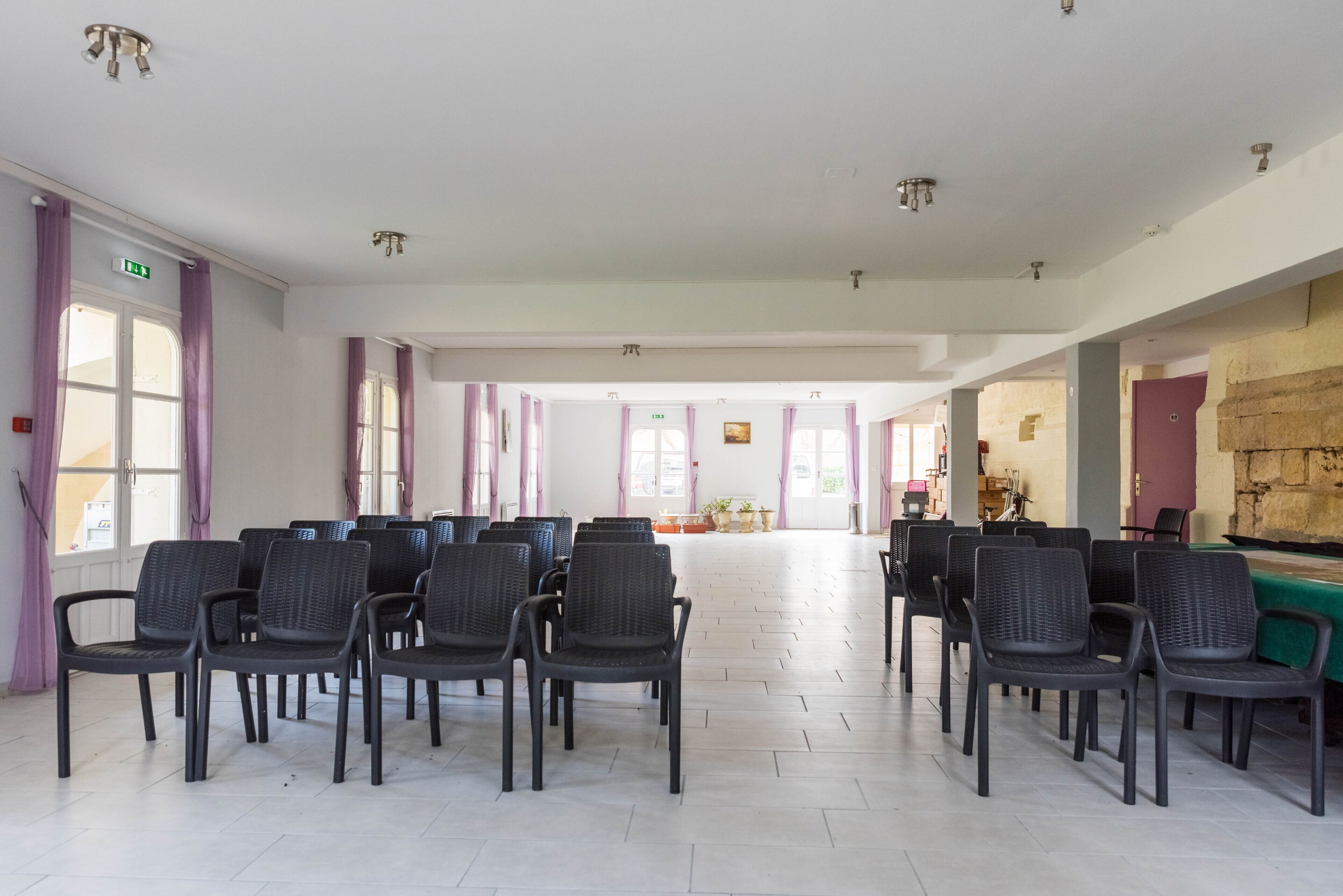 Una habitación amplia con filas de sillas dispuestas para sentarse, una mesa de billar y una señal de salida visible.