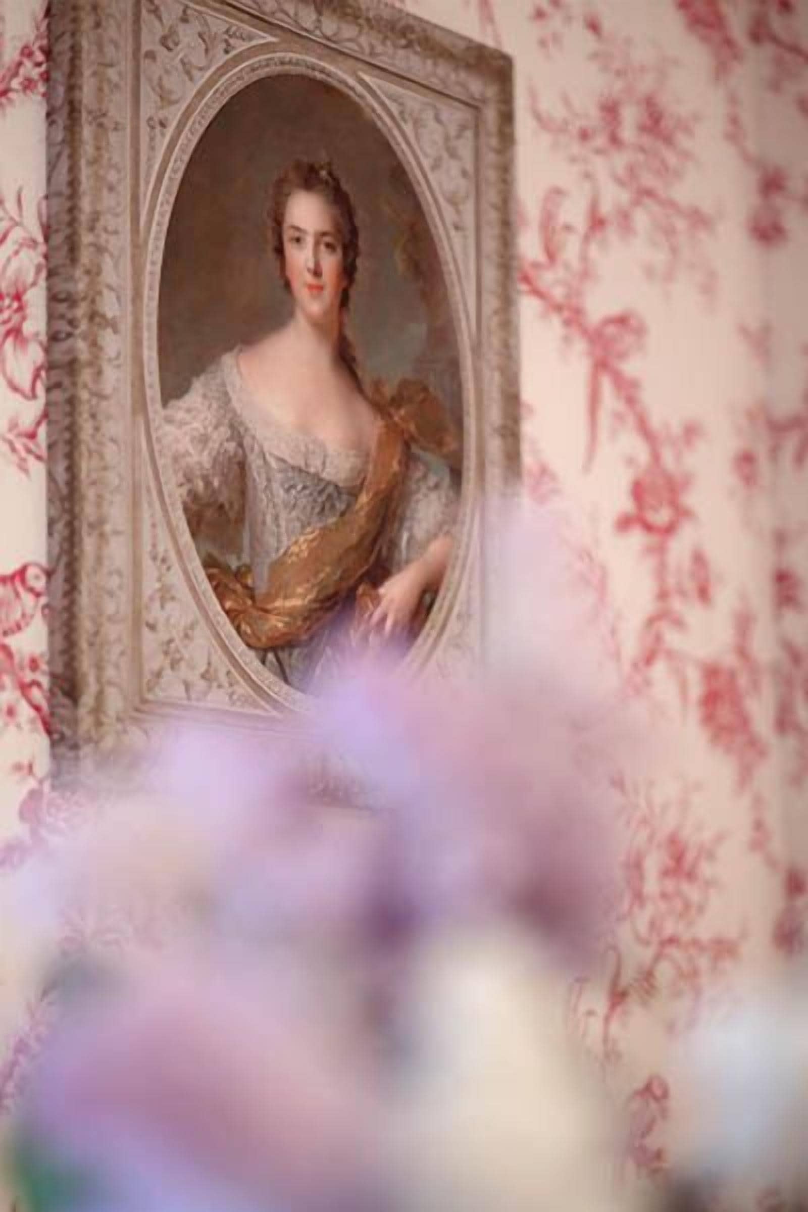 A portrait framed in an ornate, gold-colored frame with a floral wallpaper background.
