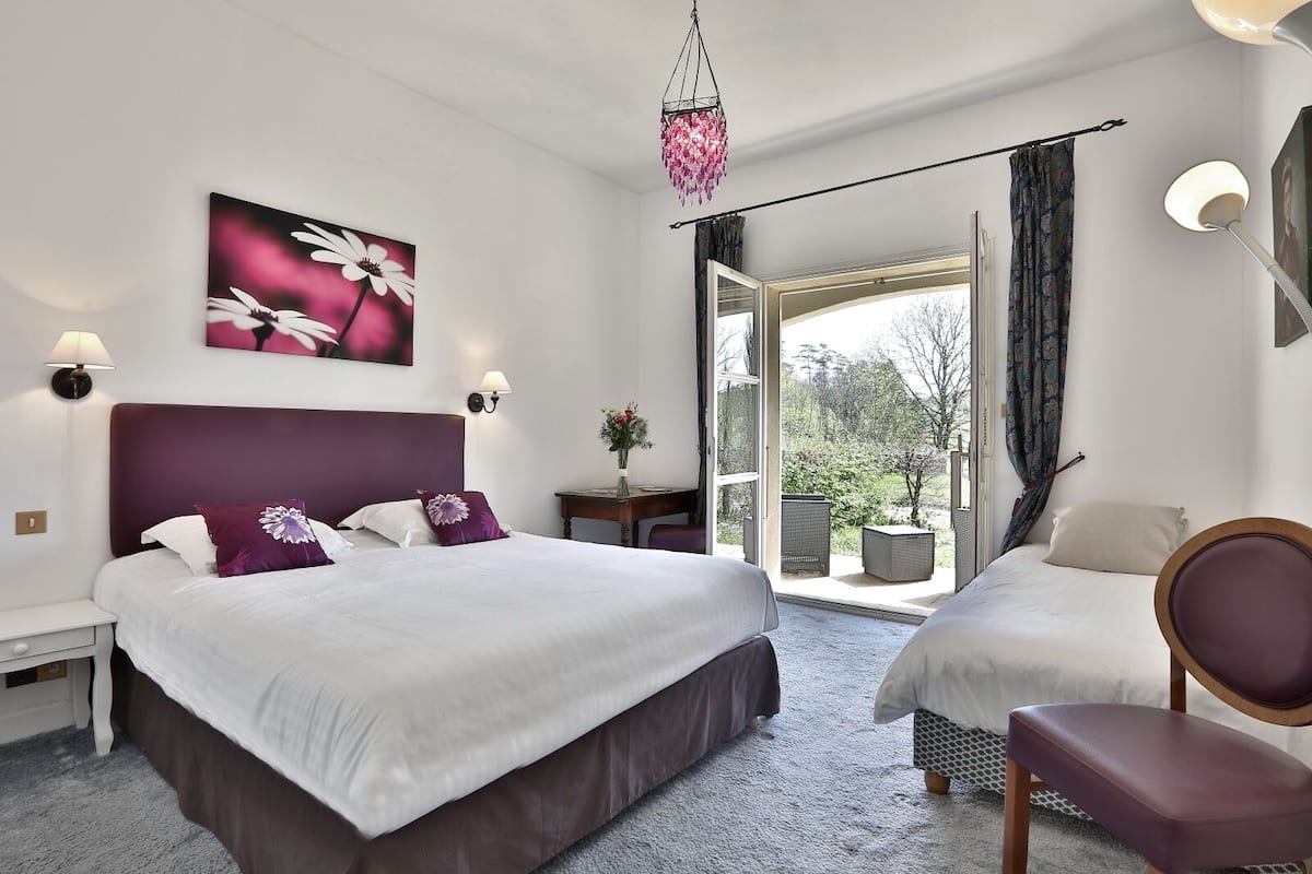 A hotel room with two beds, a chair, a desk, and a view of the outdoors.