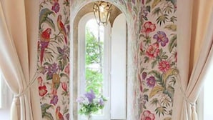 Una habitación con papel tapiz floral, un sillón rosa, una mesa con un jarrón de flores y una botella de champán.