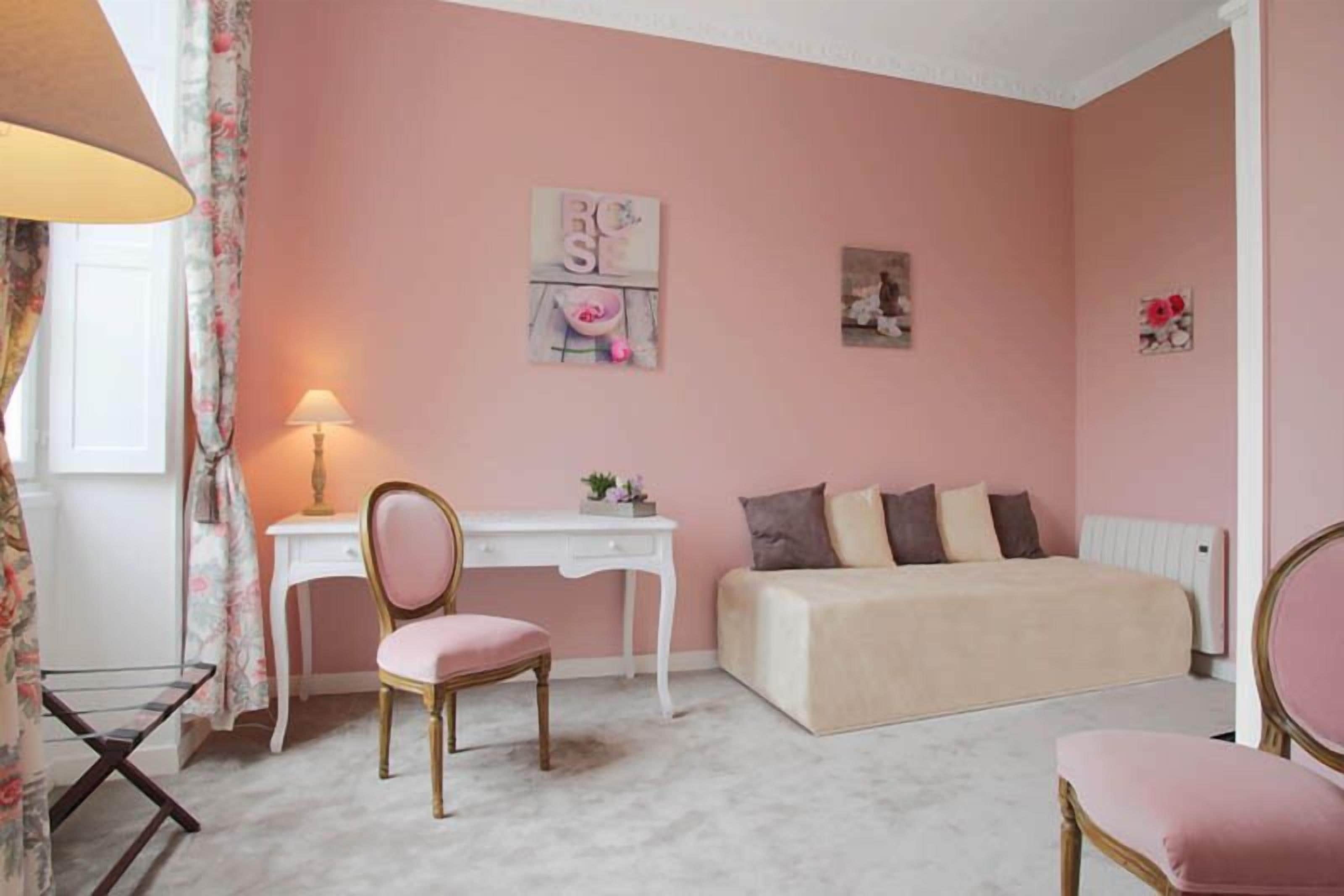 Camera da letto a tema rosa con un letto, una scrivania, una sedia e un termosifone.