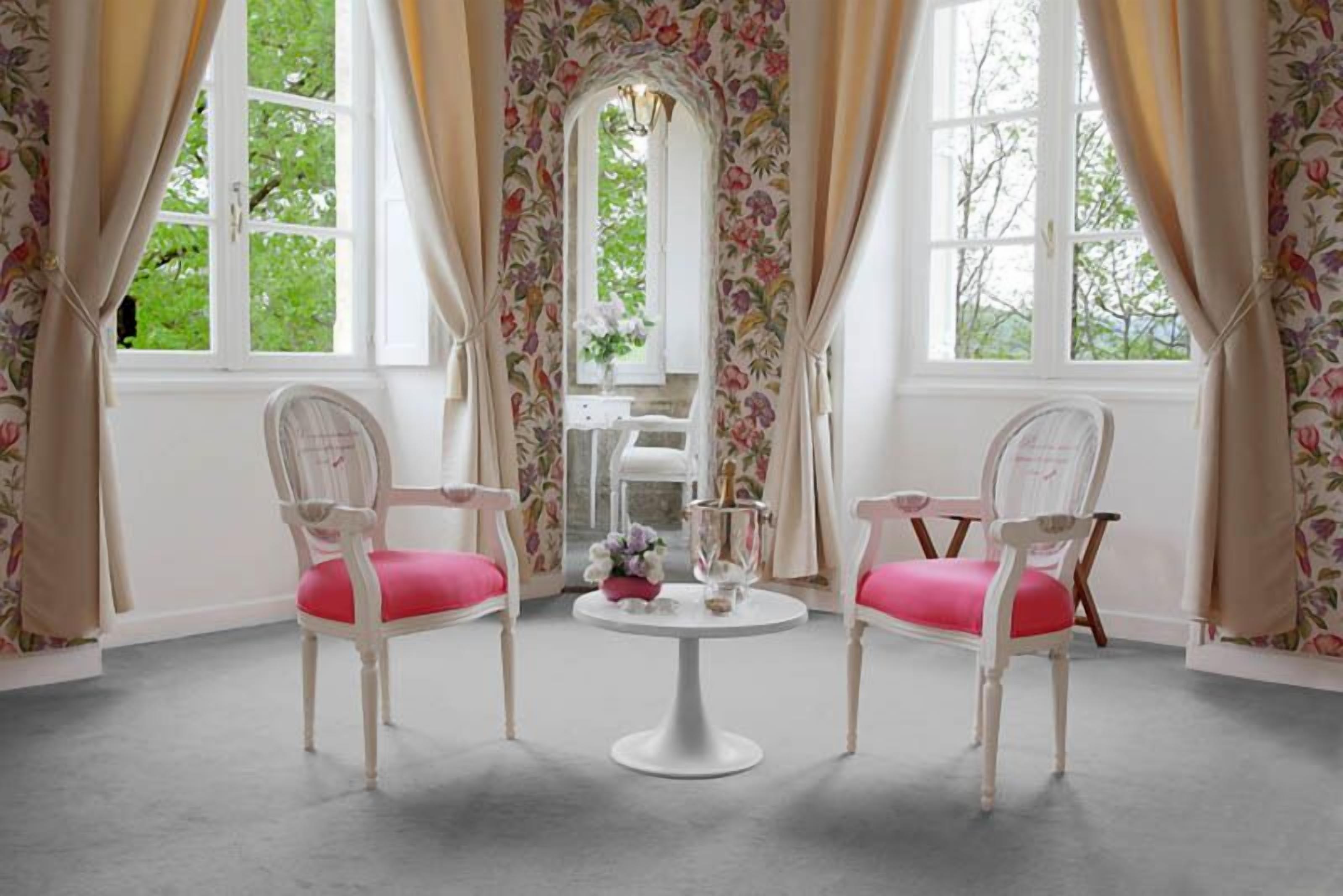 Una stanza con due sedie bianche dotate di cuscini rosa, un tavolino rotondo e carta da parati a motivi floreali.