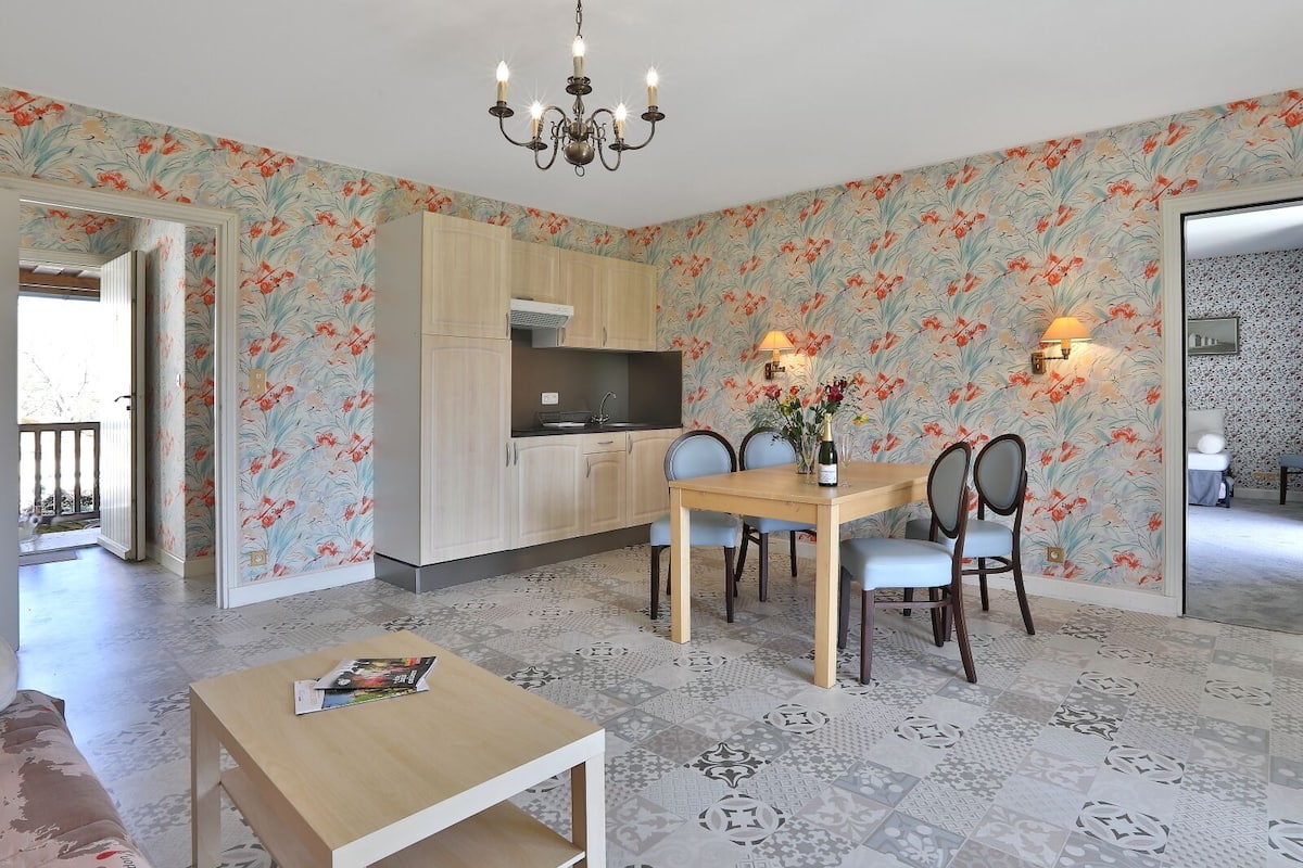 A dining area with a wooden table and chairs, a chandelier, and a floral wallpaper design.
