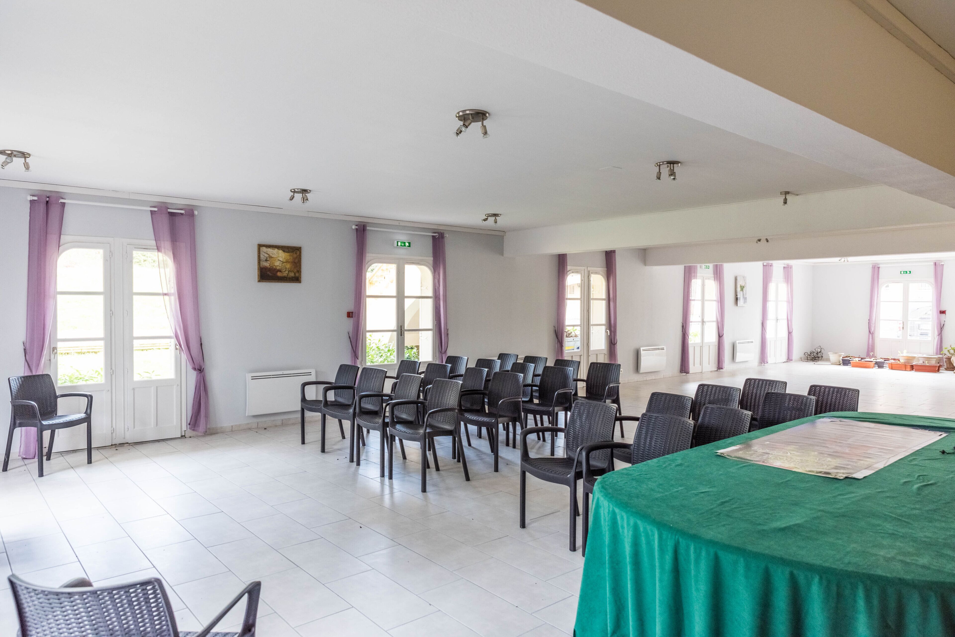 A conference room with rows of chairs, a green table, and large windows with purple curtains.