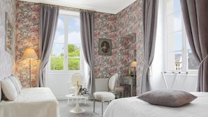 Un dormitorio con papel tapiz floral, una cama, un escritorio y una silla.