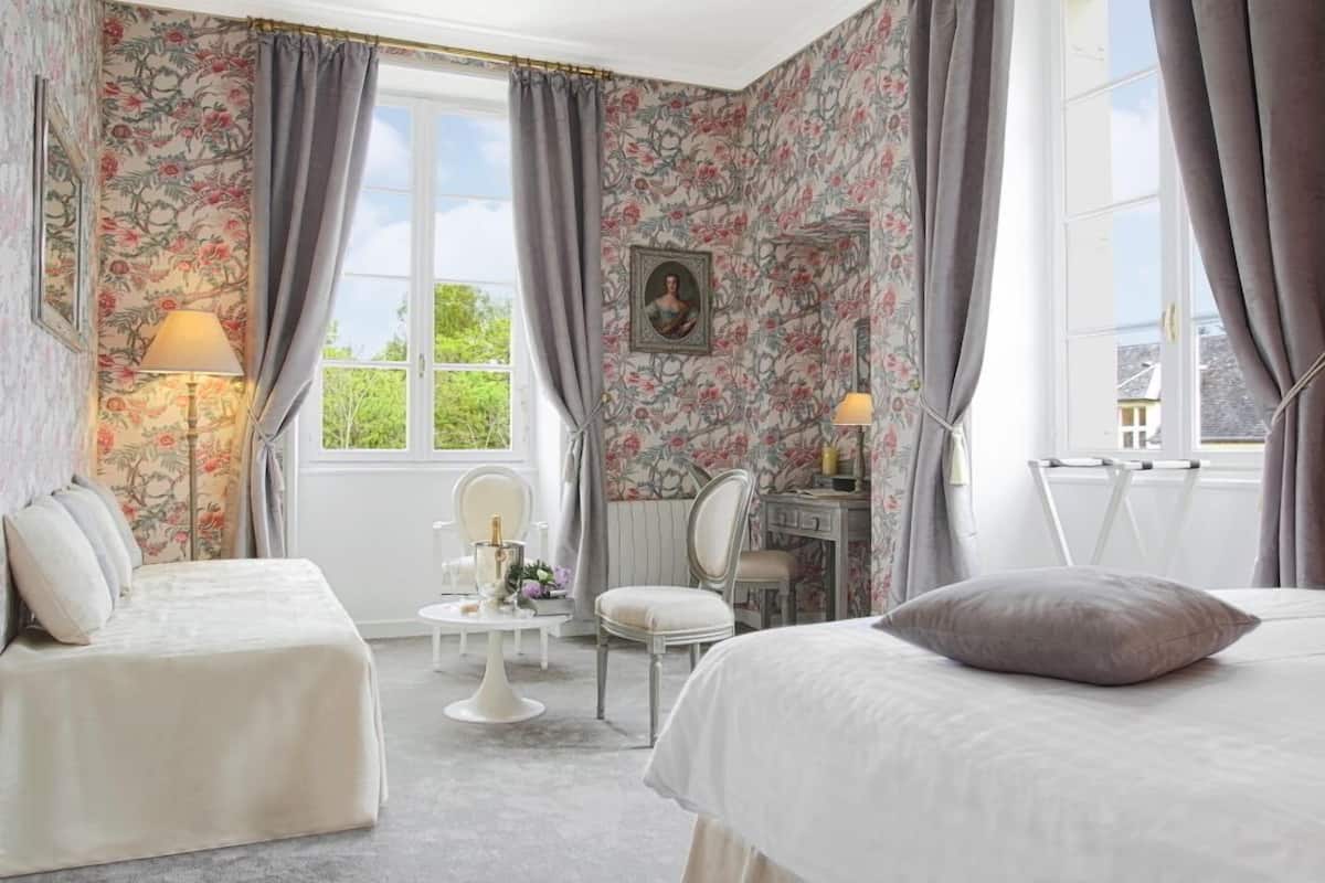 A bedroom with floral wallpaper, a bed, a desk, and a chair.