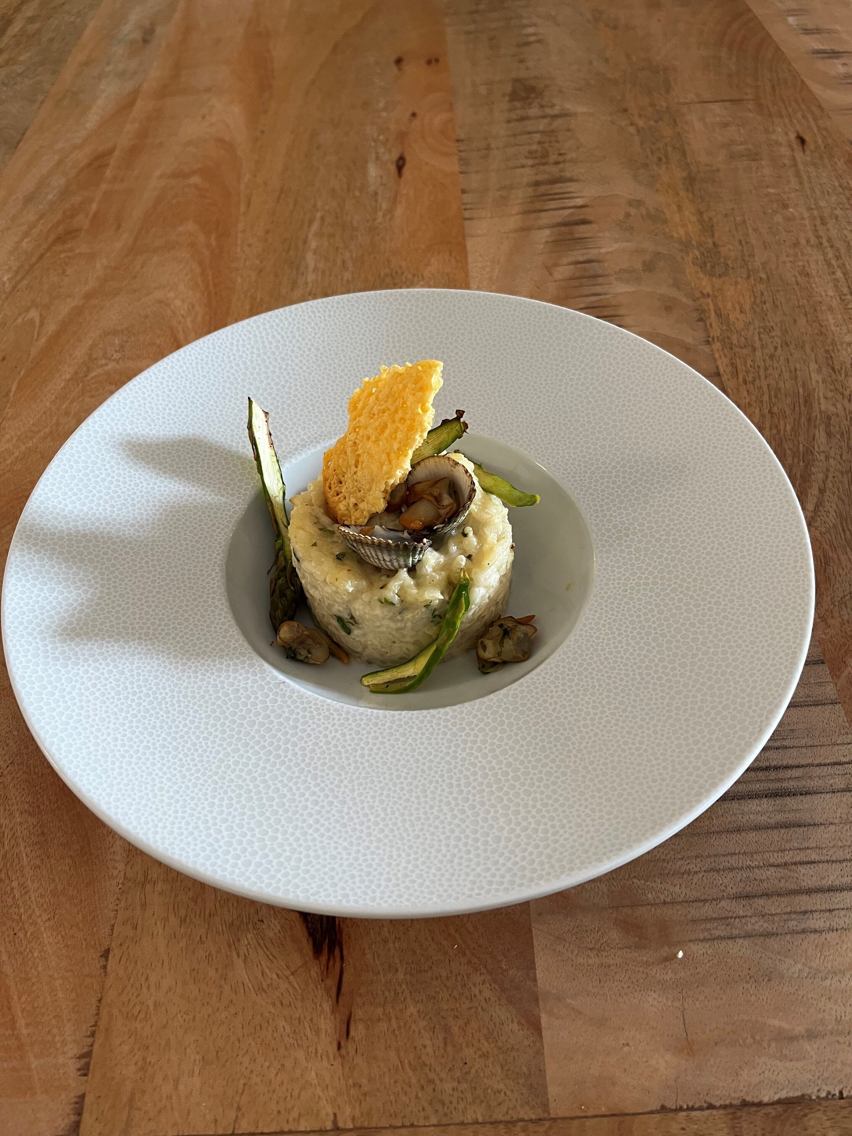 Une assiette blanche contenant un plat de fruits de mer, notamment des moules et des légumes verts, est posée sur une table en bois.