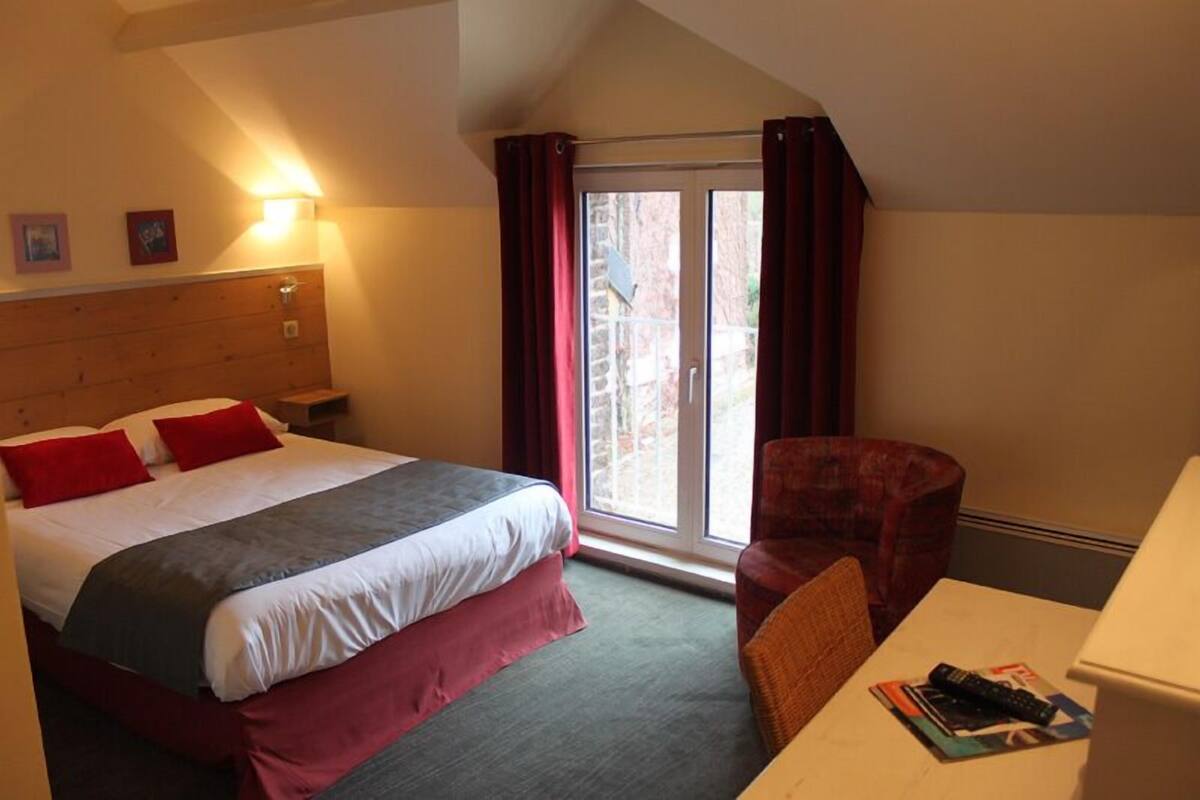 A hotel room with a bed, a chair, a table, a lamp, and a window with curtains.