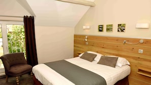 Un dormitorio con cama, una silla, cabecera de madera y un ventanal con cortinas.