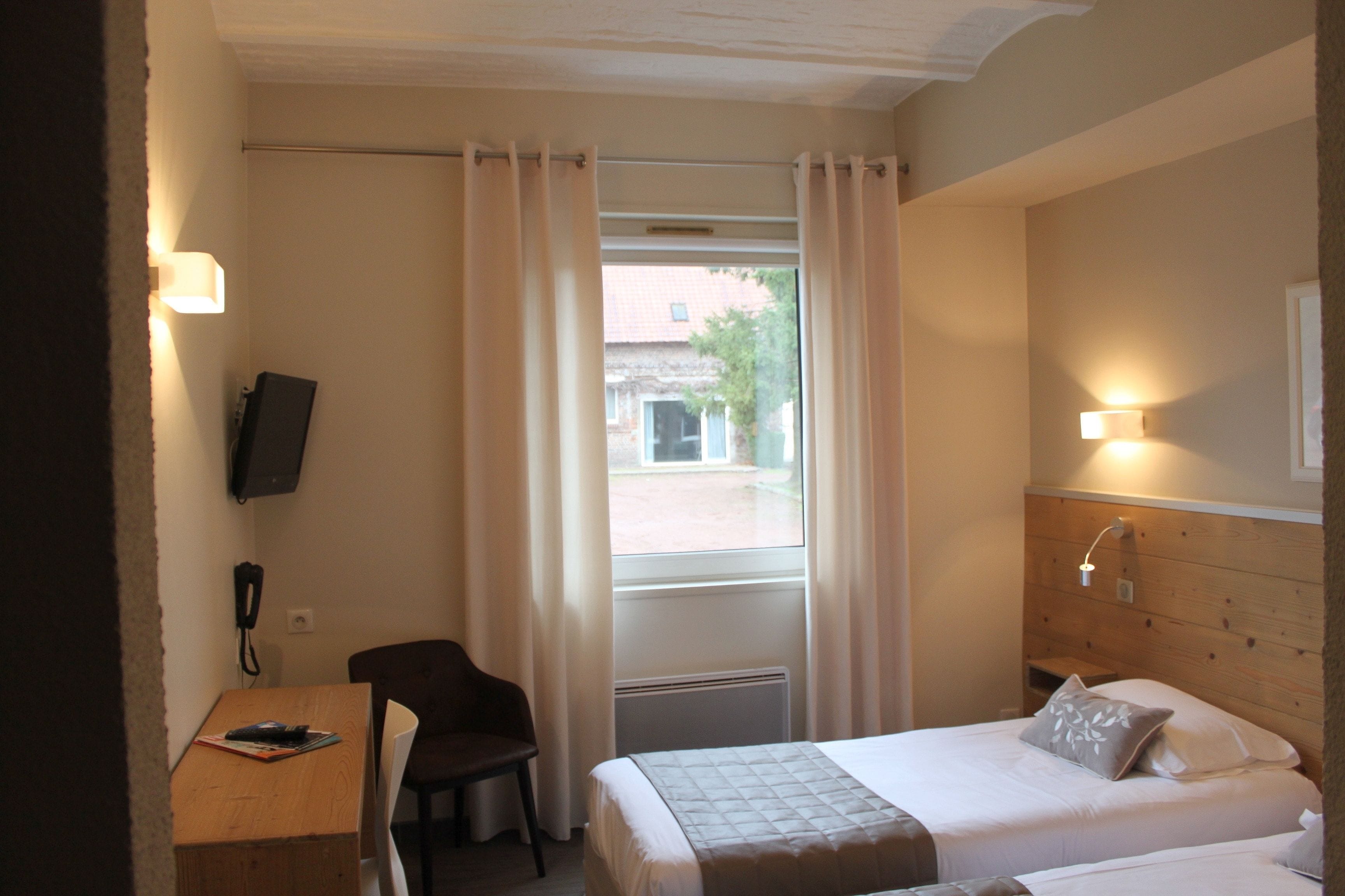 Habitación de hotel con cama, escritorio, silla, televisor y ventana con cortinas.