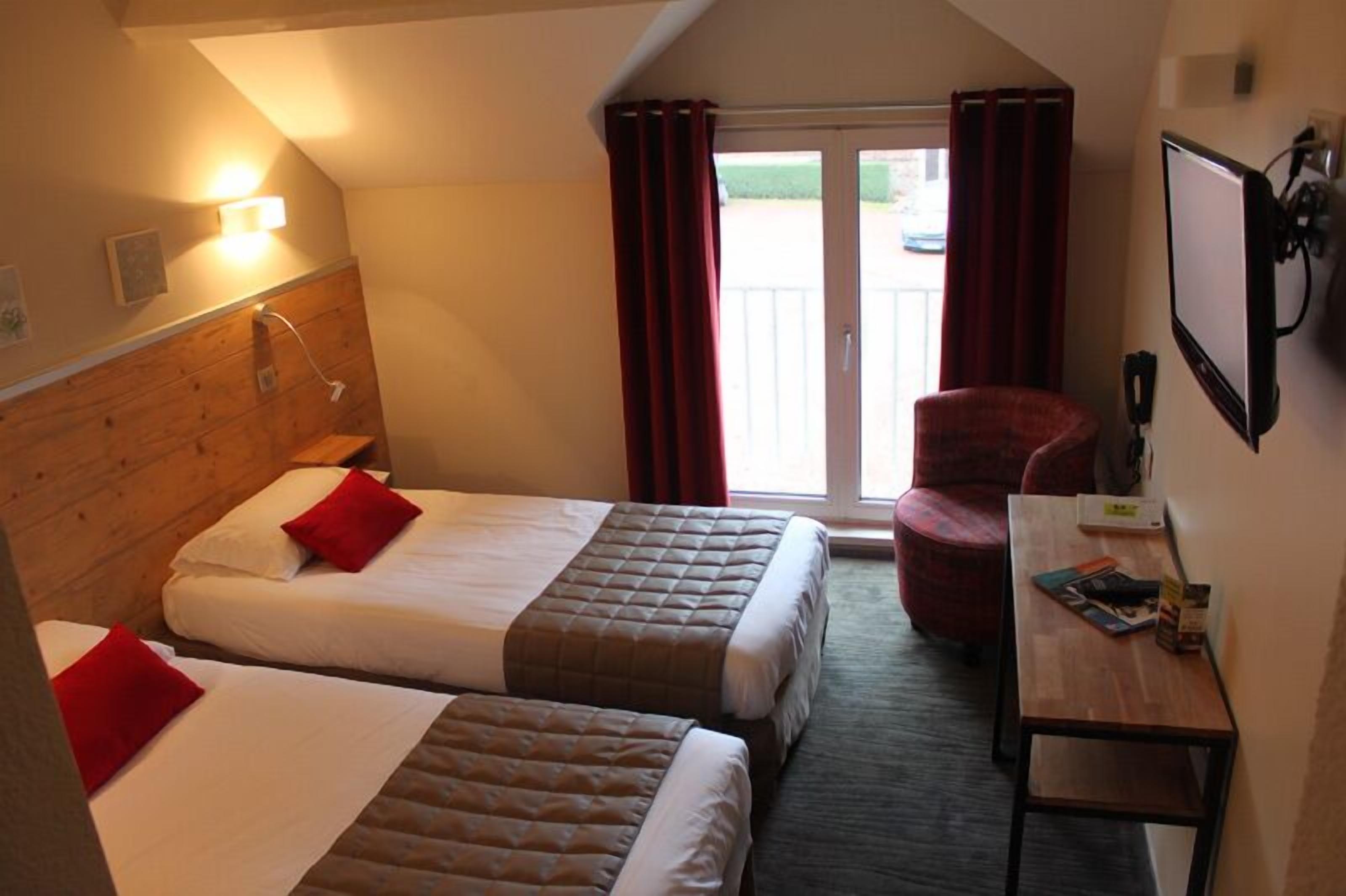 Une chambre d’hôtel avec deux lits, une tête de lit en bois, un bureau, une chaise et une vue sur l’extérieur.