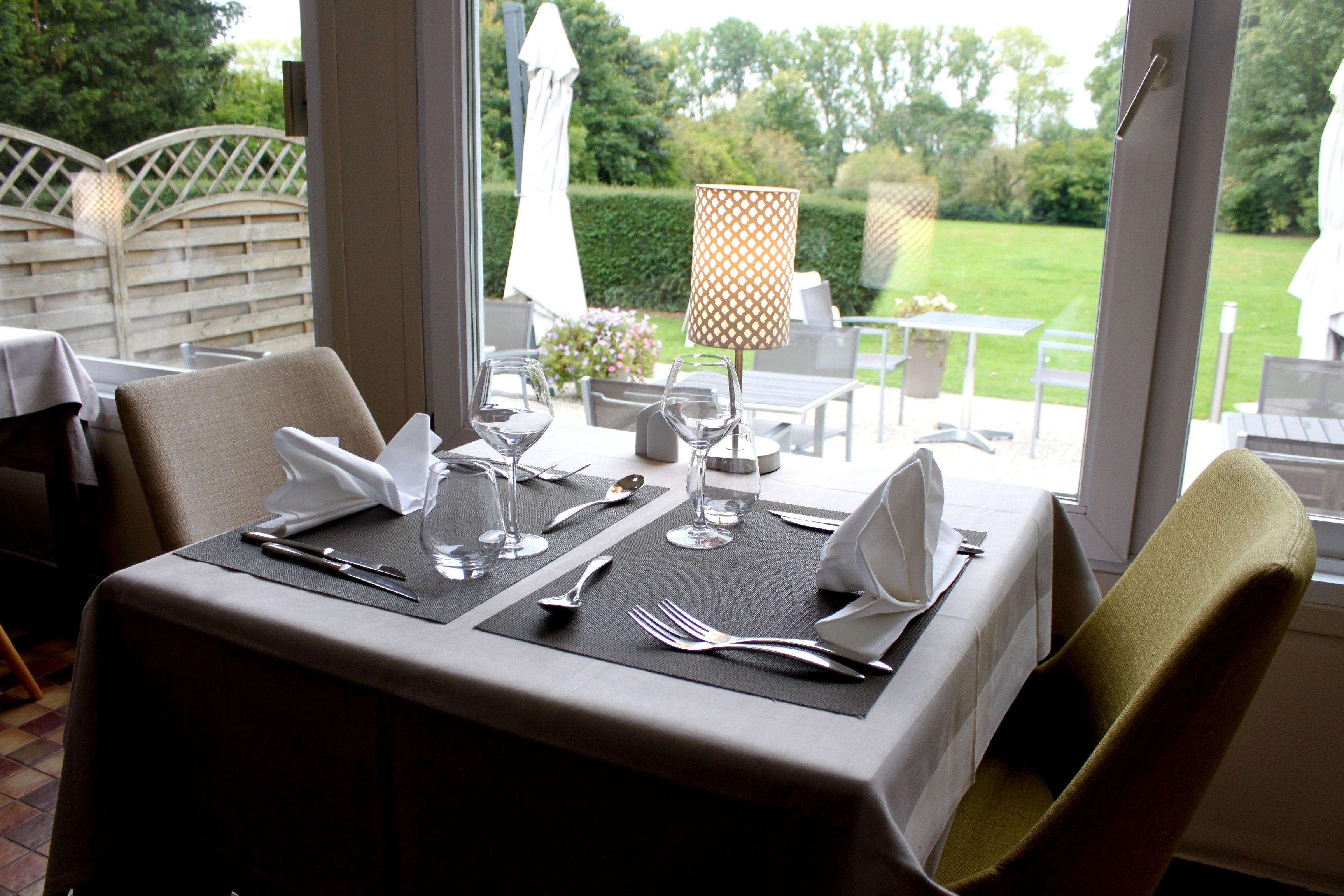 A dining table set for two with a view of a garden.
