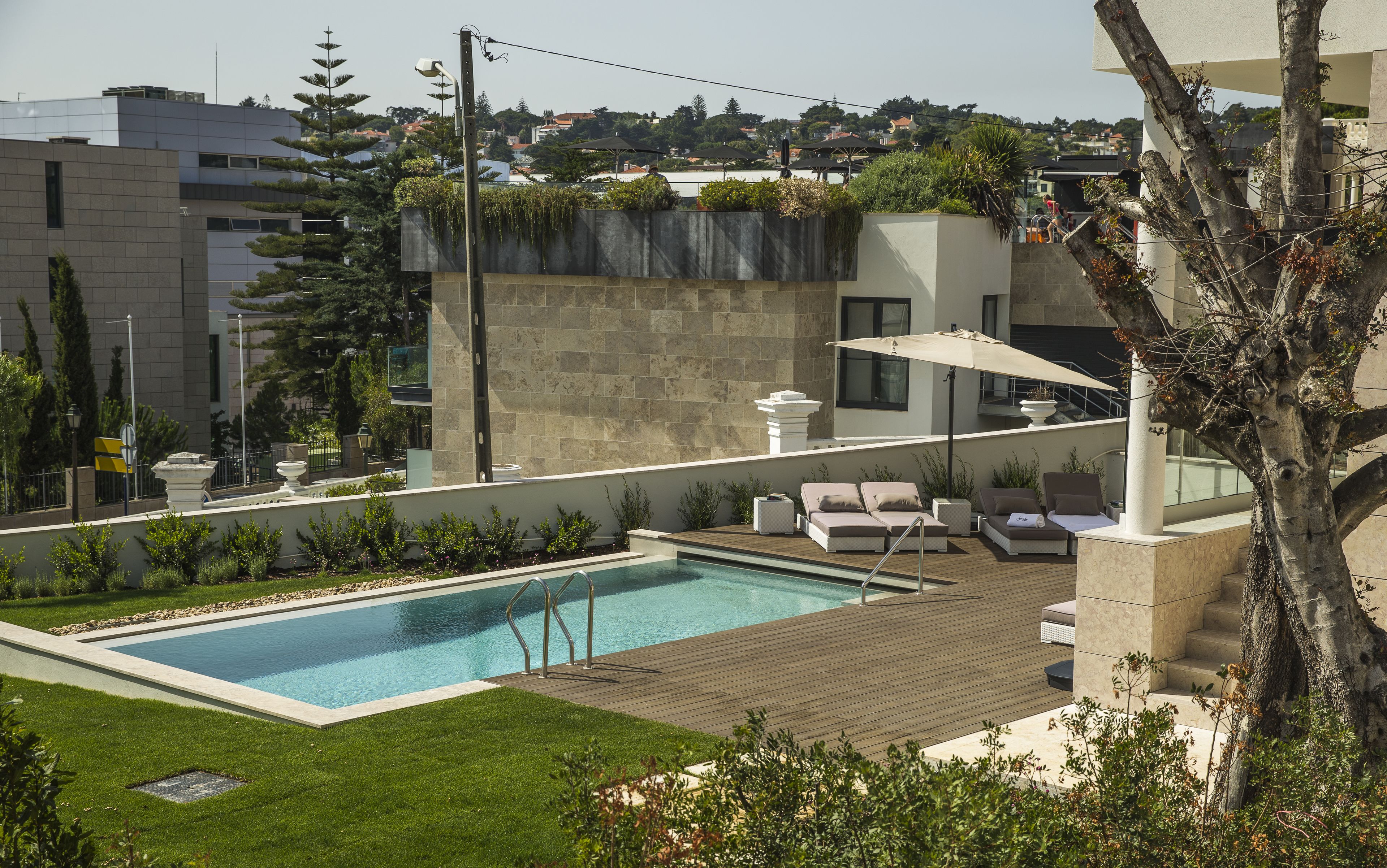 Uma área de piscina no terraço com deck de madeira, espreguiçadeiras e vista para a paisagem urbana.