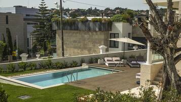Uma área de piscina no terraço com deck de madeira, espreguiçadeiras e vista para a paisagem urbana.