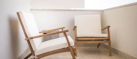 Twee houten stoelen met witte kussens in een hoek van een kamer met betegelde vloer en witte wanden.