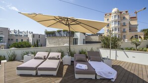 Zona de lounge en la azotea con dos tumbonas, un parasol grande y vistas de un edificio en construcción.