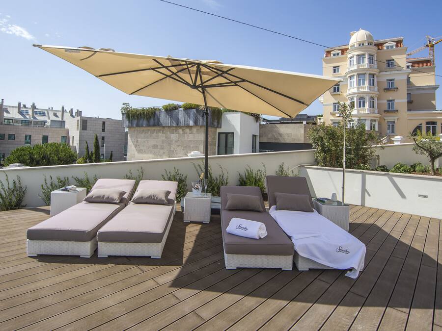 Zona de lounge en la azotea con dos tumbonas, un parasol grande y vistas de un edificio en construcción.