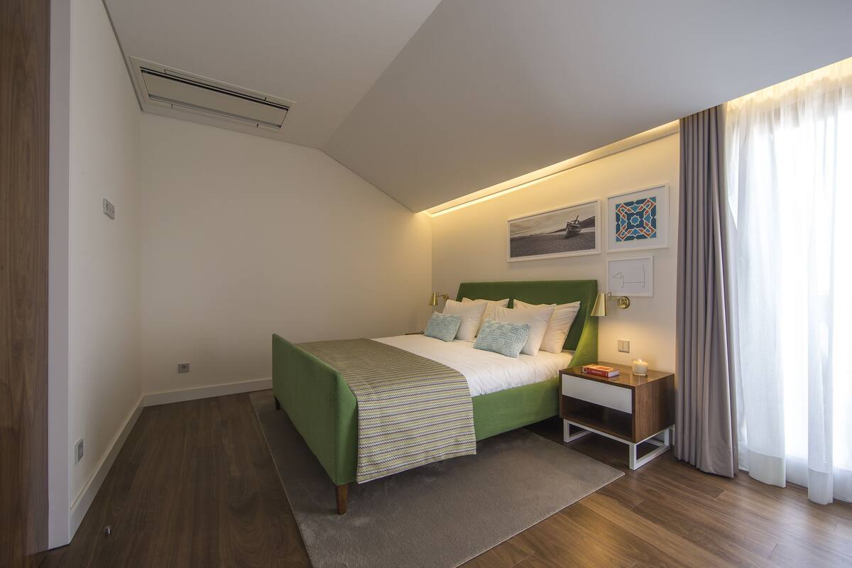 Un dormitorio moderno con una cama verde, ropa de cama blanca, una mesita de noche y una lámpara de noche.
