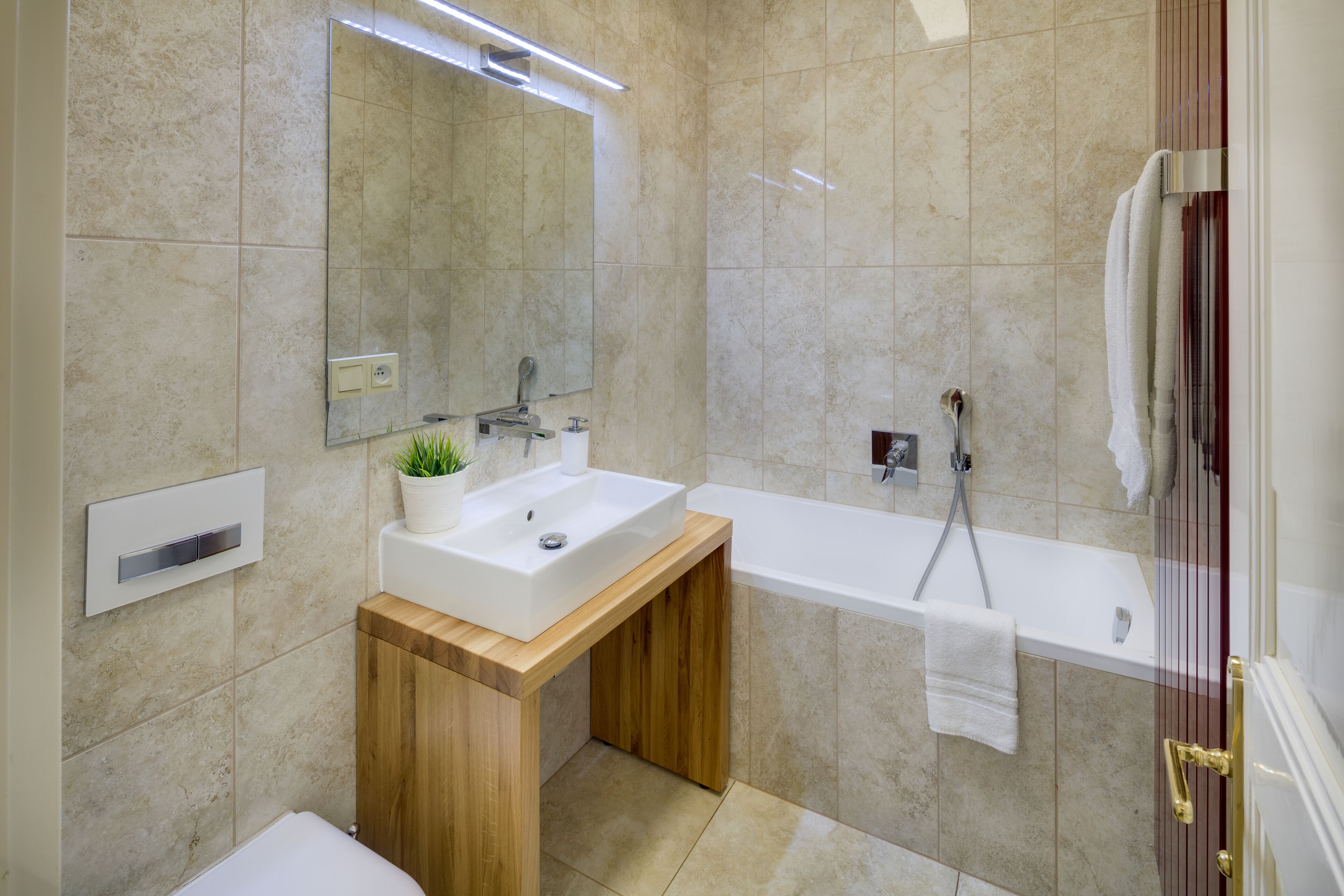 A modern bathroom with a white sink, wooden vanity, a large mirror, and a bathtub.
