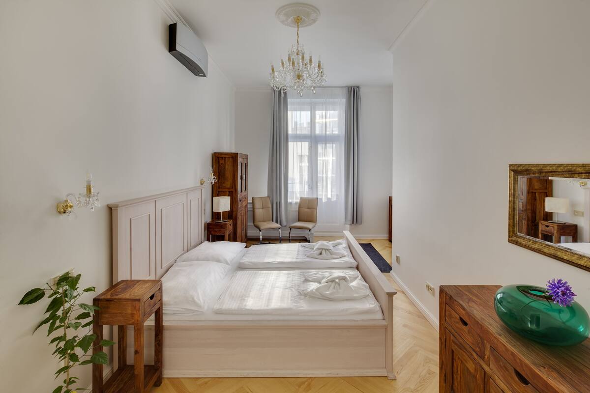 Ein Hotelzimmer mit einem großen Bett, einem Nachttisch aus Holz, einer grünen Vase und einem Spiegel an der Wand.