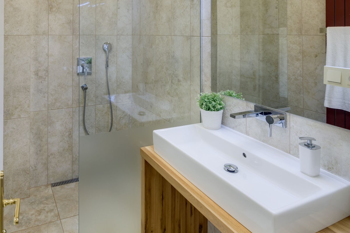 Ein modernes Badezimmer mit einer gläsernen Duschkabine, einem hölzernen Waschtisch mit weißem Becken und einem Spiegel darüber.