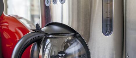 Una cafetera Kenwood con un depósito de agua transparente, panel de control y cable de alimentación sobre una encimera.