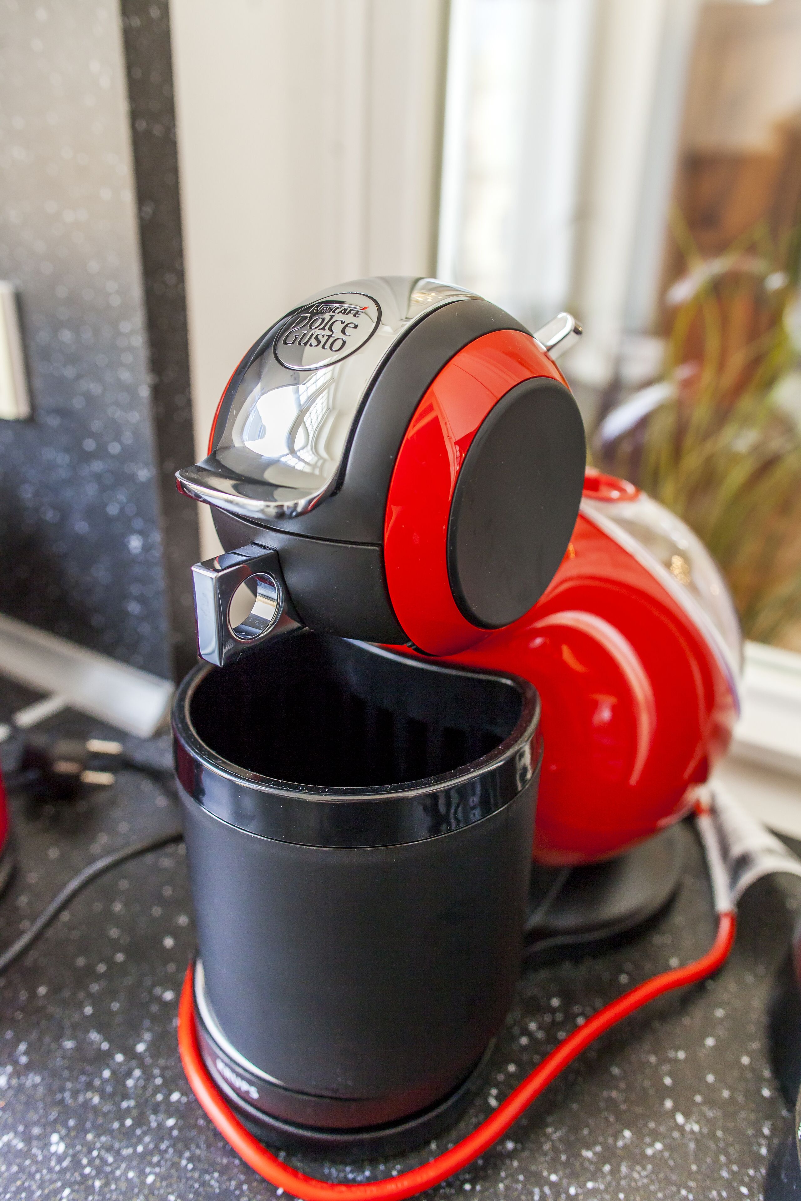 A red and black coffee machine with a cup placed underneath it.