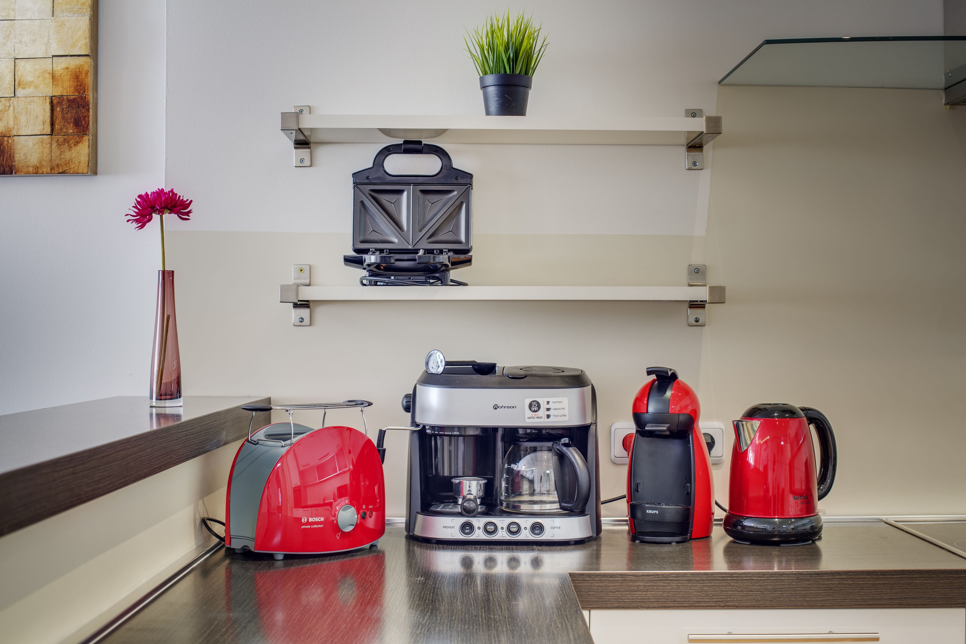Eine Küche mit Kaffeemaschine, Toaster, Wasserkocher und einer Topfpflanze auf der Arbeitsfläche.