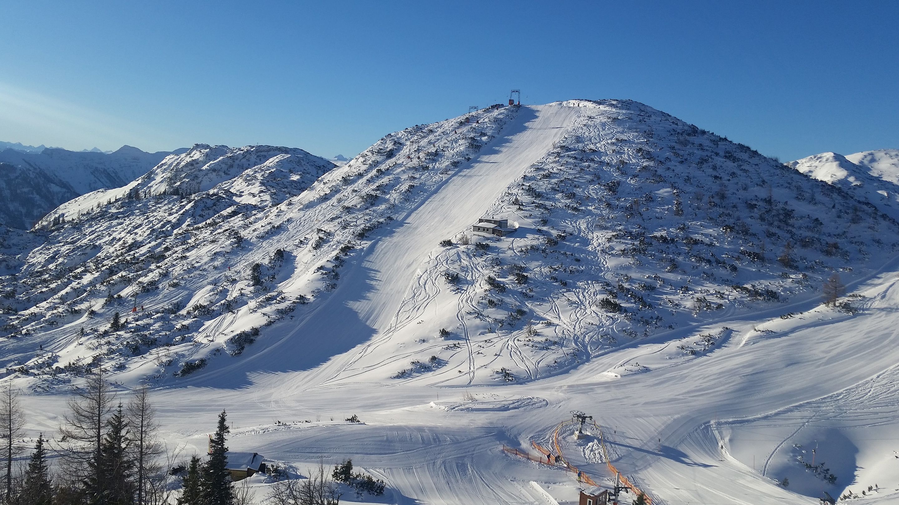 Une montagne enneigée, avec des pistes de ski et un petit bâtiment au sommet.