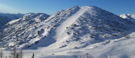 Une montagne enneigée, avec des pistes de ski et un petit bâtiment au sommet.