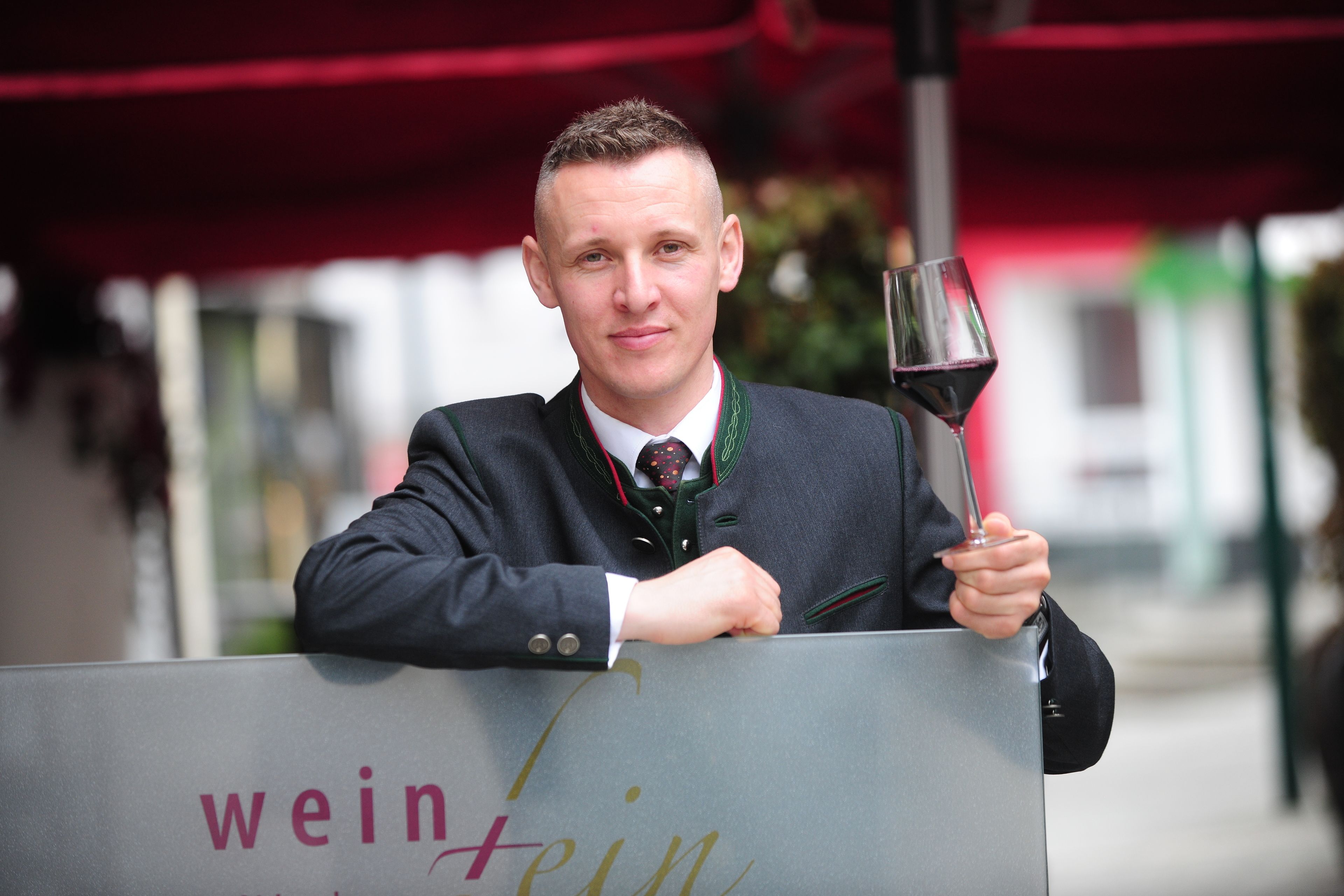 A person holding a wine glass and a sign with "wein fein" text.