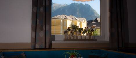 Una habitación con una mesa lista para comer, una ventana con vistas a montañas, un sofá con cojines estampados y una lámpara colgante.