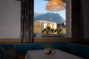 Une pièce avec une table dressée pour le repas, une fenêtre donnant sur les montagnes, un canapé agrémenté de coussins à motifs et un luminaire suspendu.