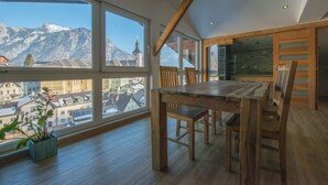Amplia habitación con grandes ventanales que ofrecen vista a la montaña, una mesa de comedor de madera y una planta en maceta.