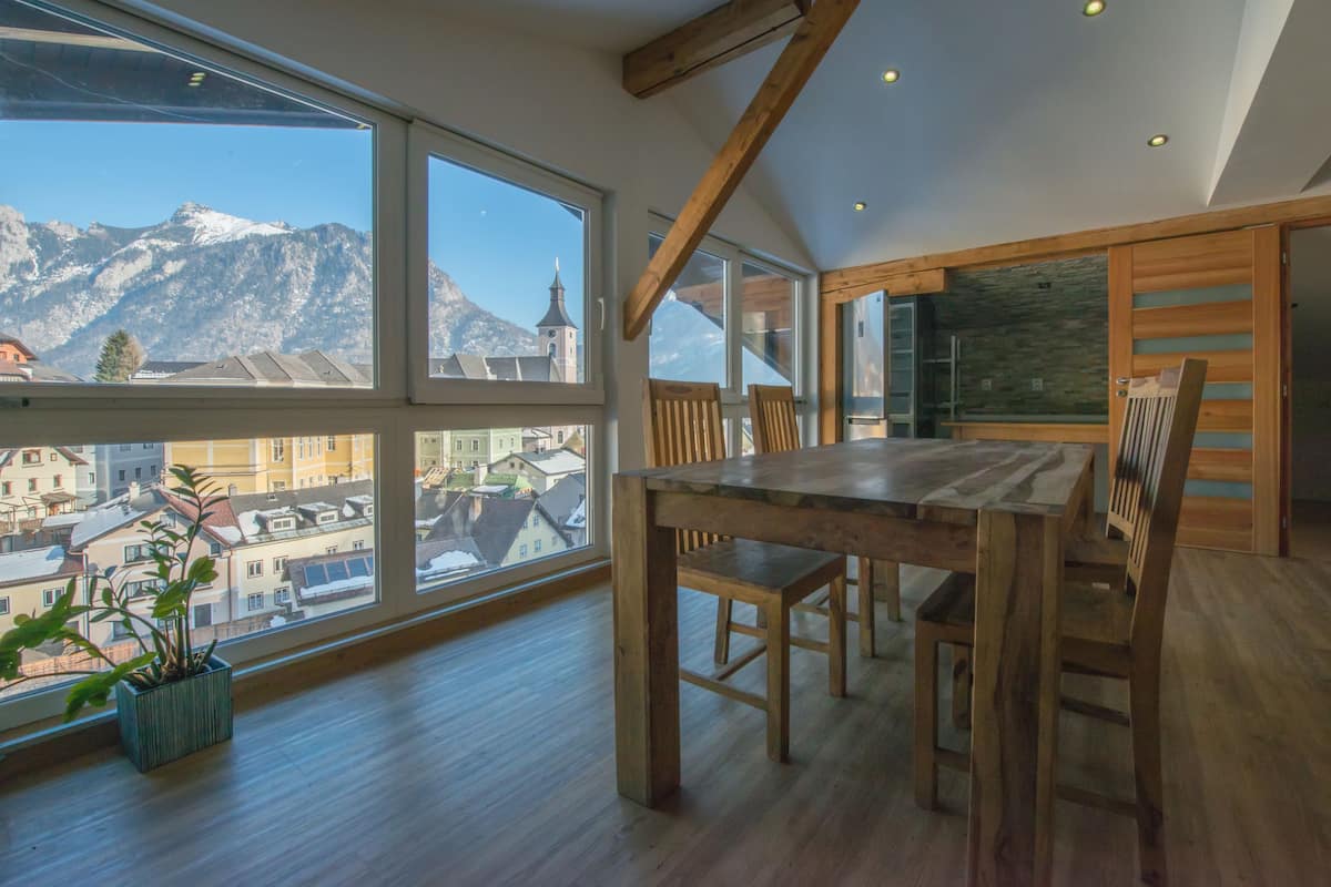 Ein geräumiger Raum mit großen Fenstern und Bergblick, einem Holzespeisetisch und einem Blumentopf.