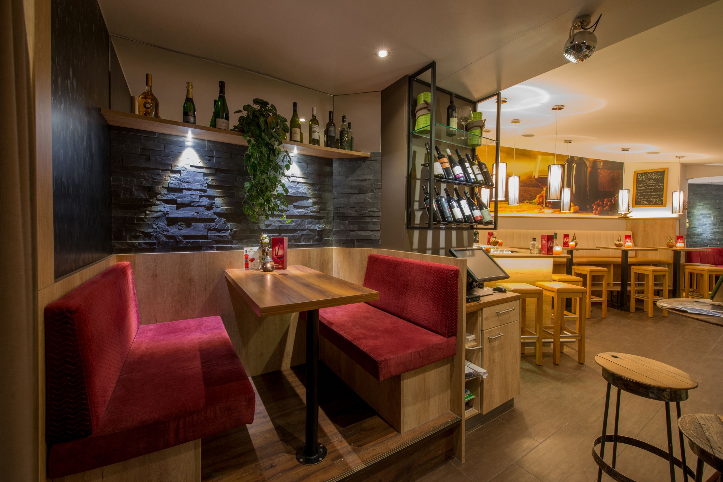 A bar area with red upholstered seating, a stone wall, and a variety of bottles on shelves.