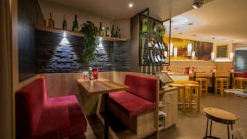 A bar area with red upholstered seating, a stone wall, and a variety of bottles on shelves.