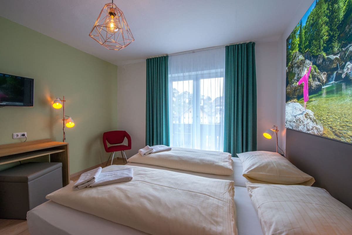 Ein Hotelzimmer mit zwei Betten, einem Schreibtisch, einem Stuhl, einem Fernseher und einem großen Fenster mit Vorhängen.