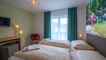 A hotel room with two beds, a desk, a chair, a TV, and a large window with curtains.