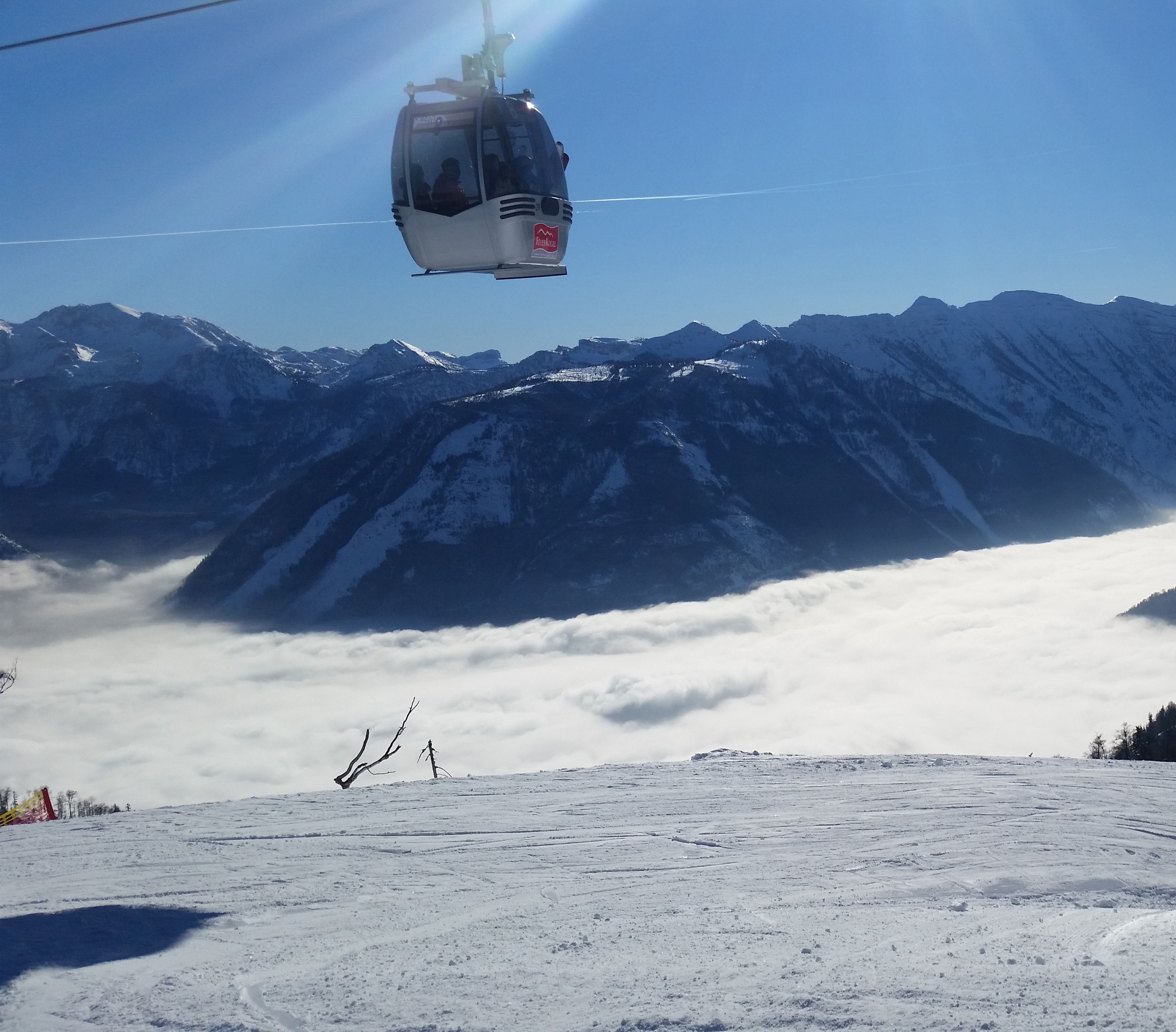 Une télécabine se déplace au-dessus d’un paysage montagneux enneigé, sous un ciel dégagé.