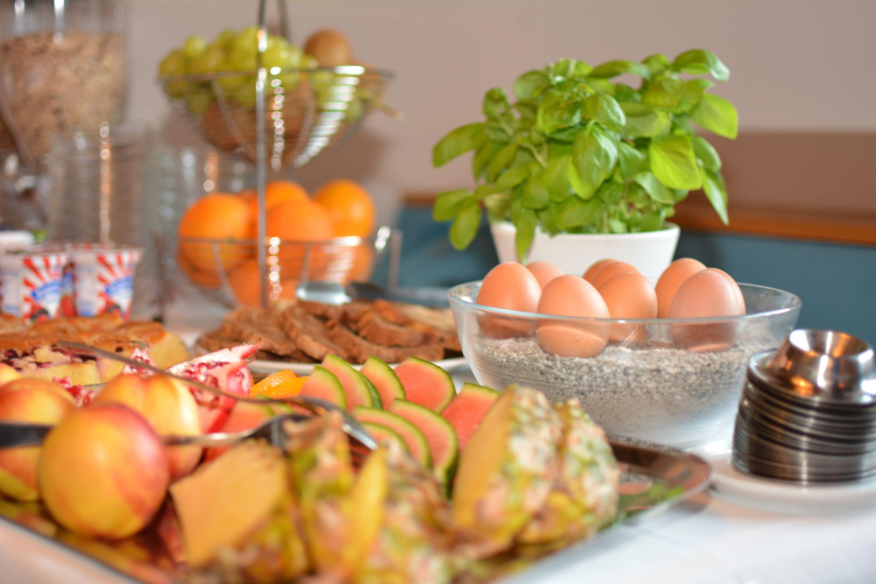 Ein Frühstücksbuffet mit verschiedenen Früchten, Eiern und einem Topfbasilikum.