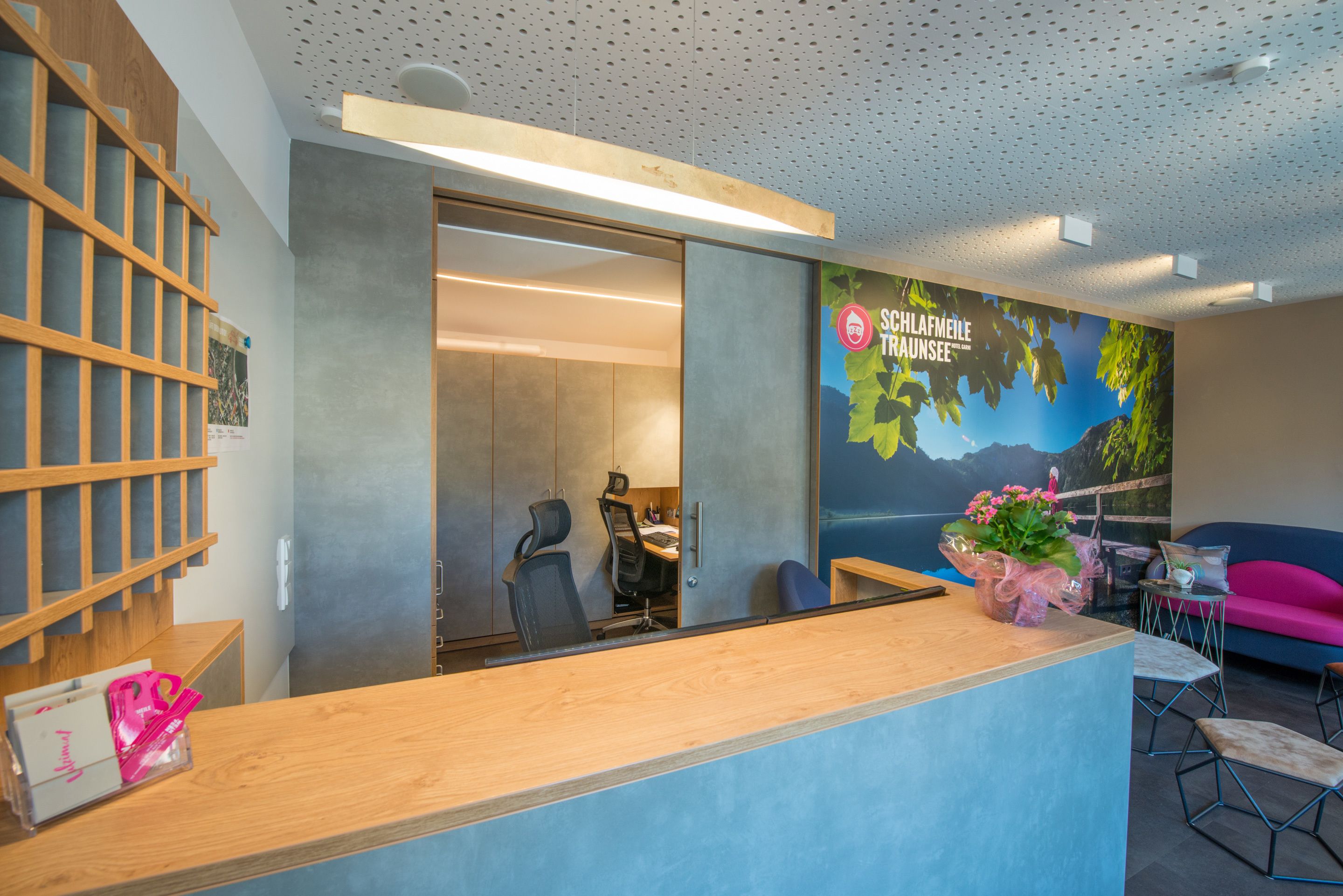 A reception desk with a wooden counter, a seating area with a blue sofa, and a wall mural depicting a mountainous landscape.