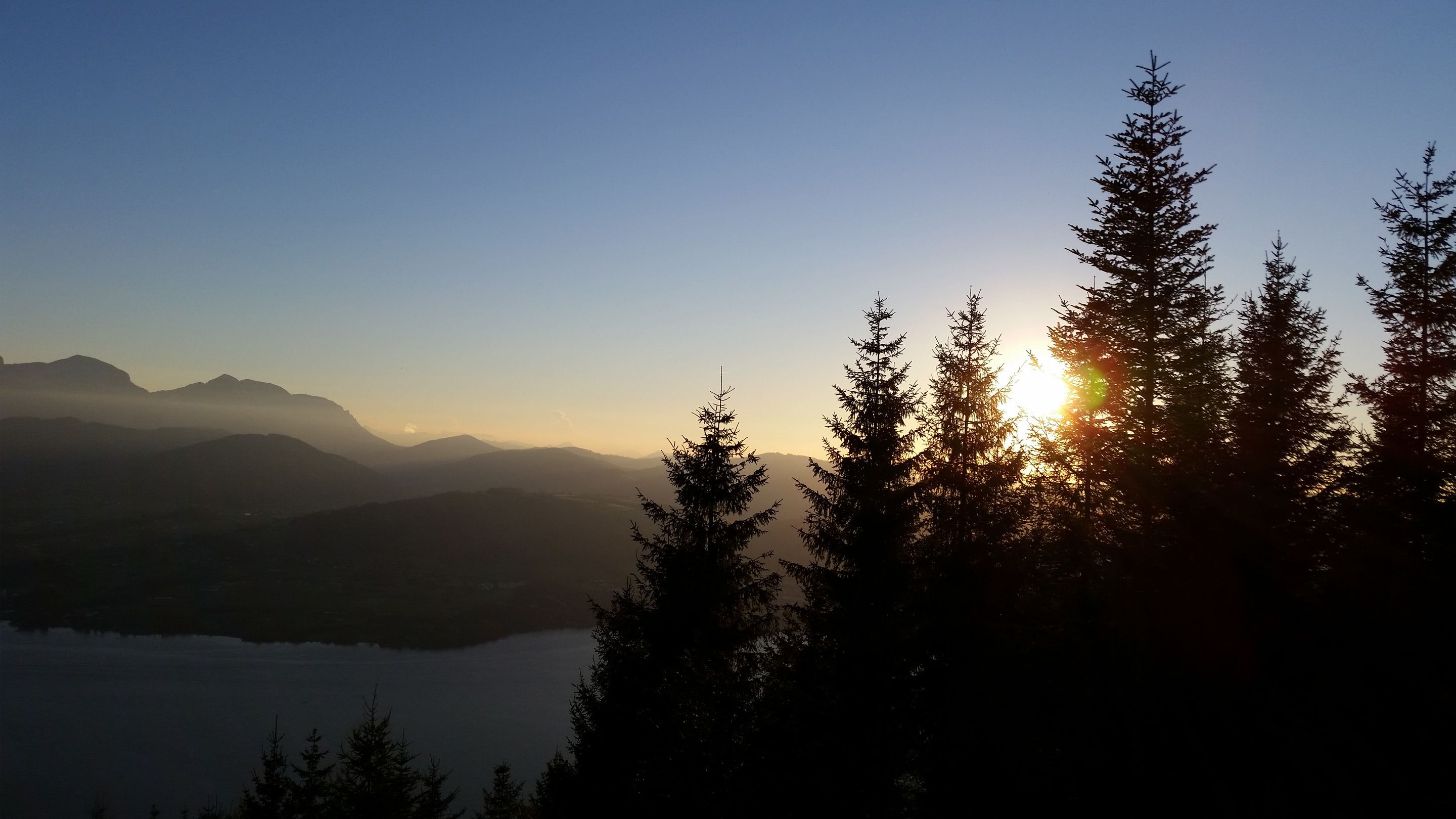 A mountainous landscape with a lake and trees in the foreground.